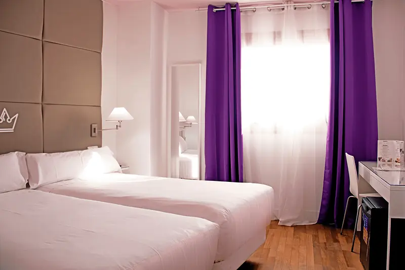 Habitación doble con dos camas, cabecero acolchado gris con corona y cortinas moradas