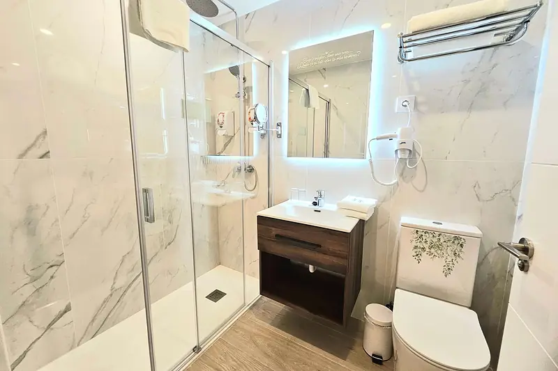 Baño de mármol blanco con ducha de lluvia, mampara y espejo iluminado