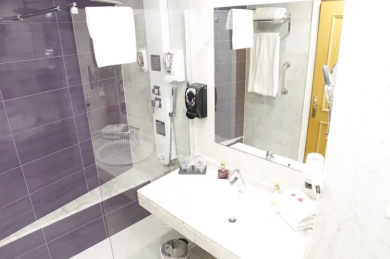 Baño con lavabo blanco, mampara de ducha y azulejos morados